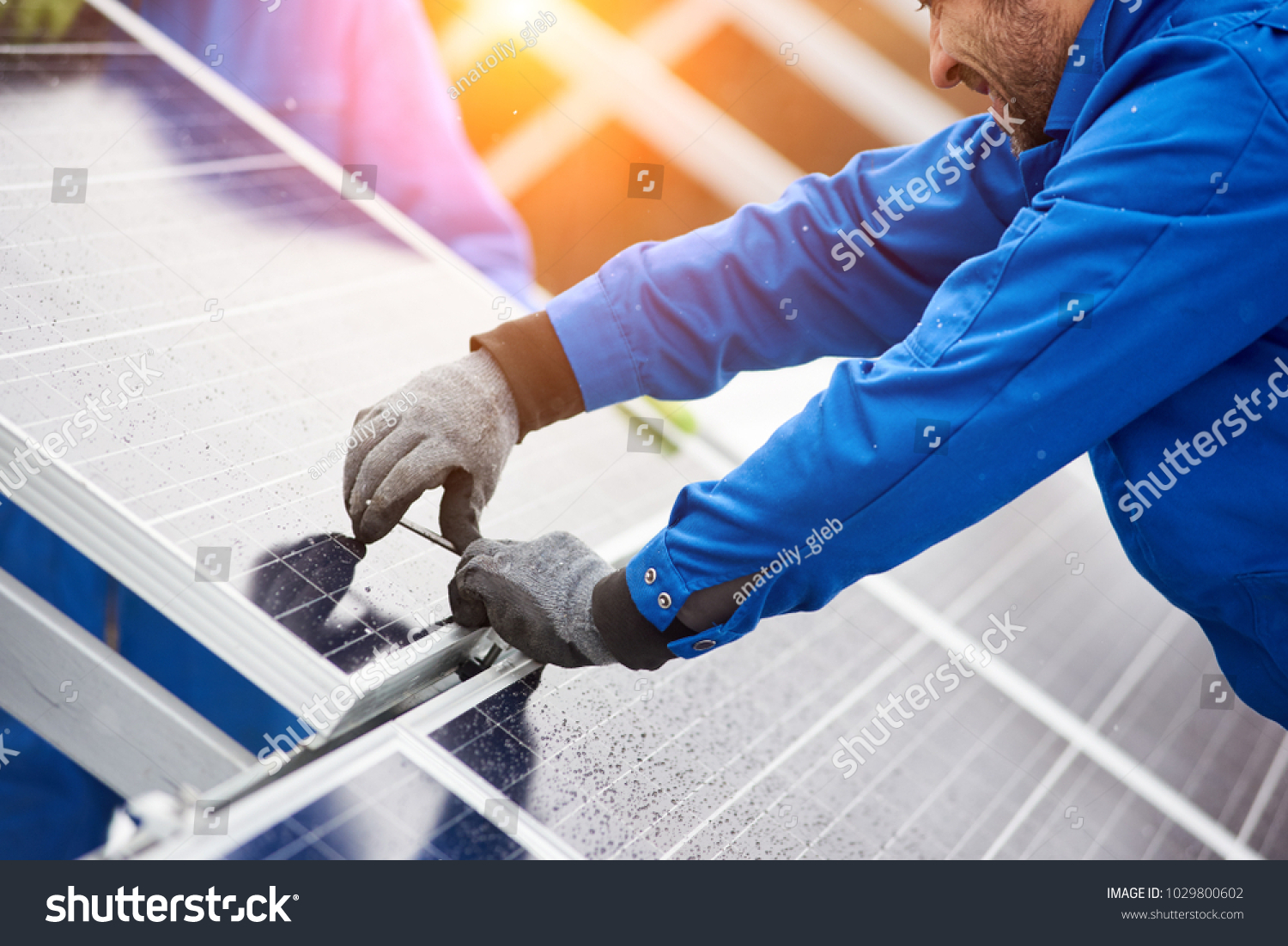 stock-photo-smiling-male-technician-in-blue-suit-installing-photovoltaic-blue-solar-modules-with-screw-man-1029800602